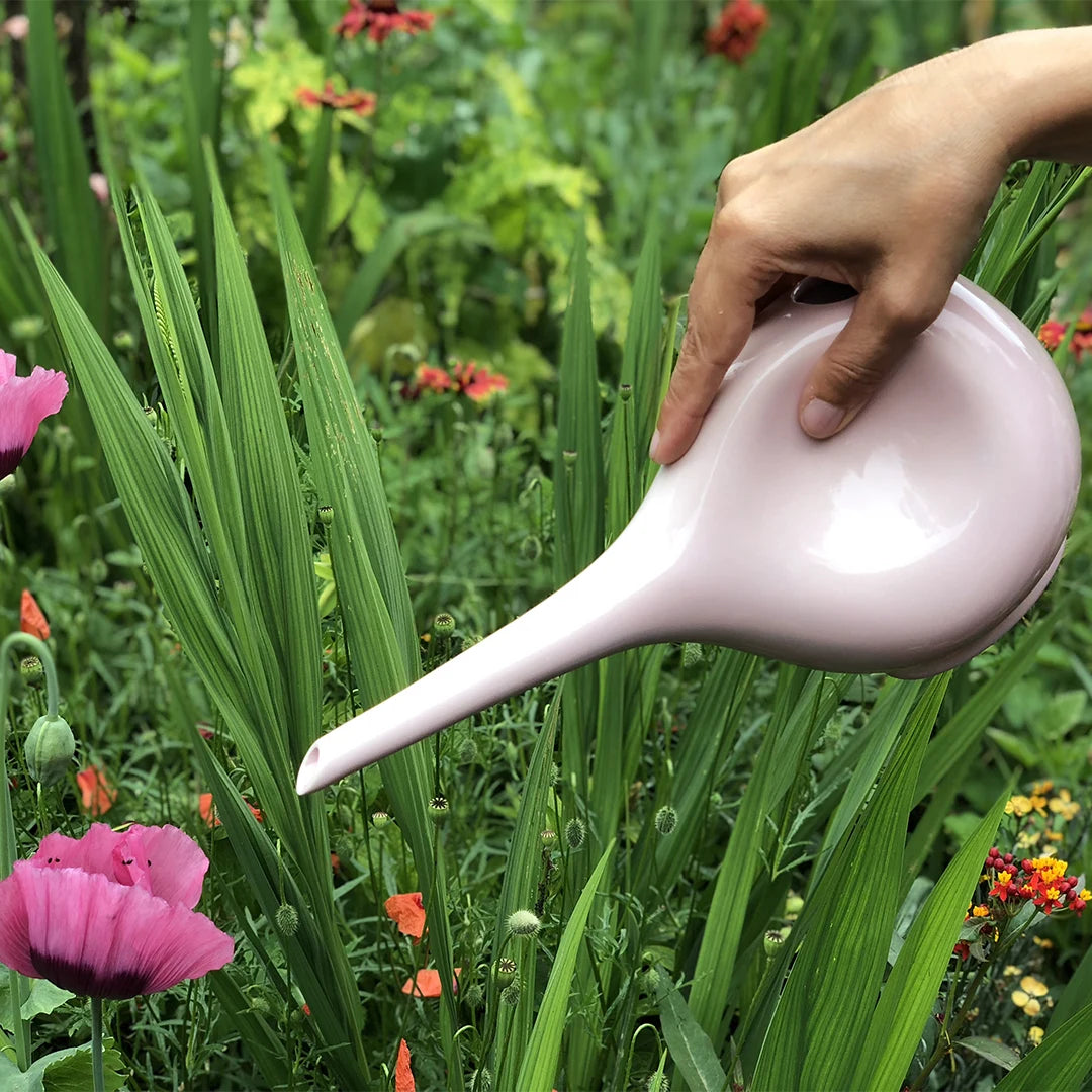 Rosafarbene Gießkanne beim Gießen im Garten